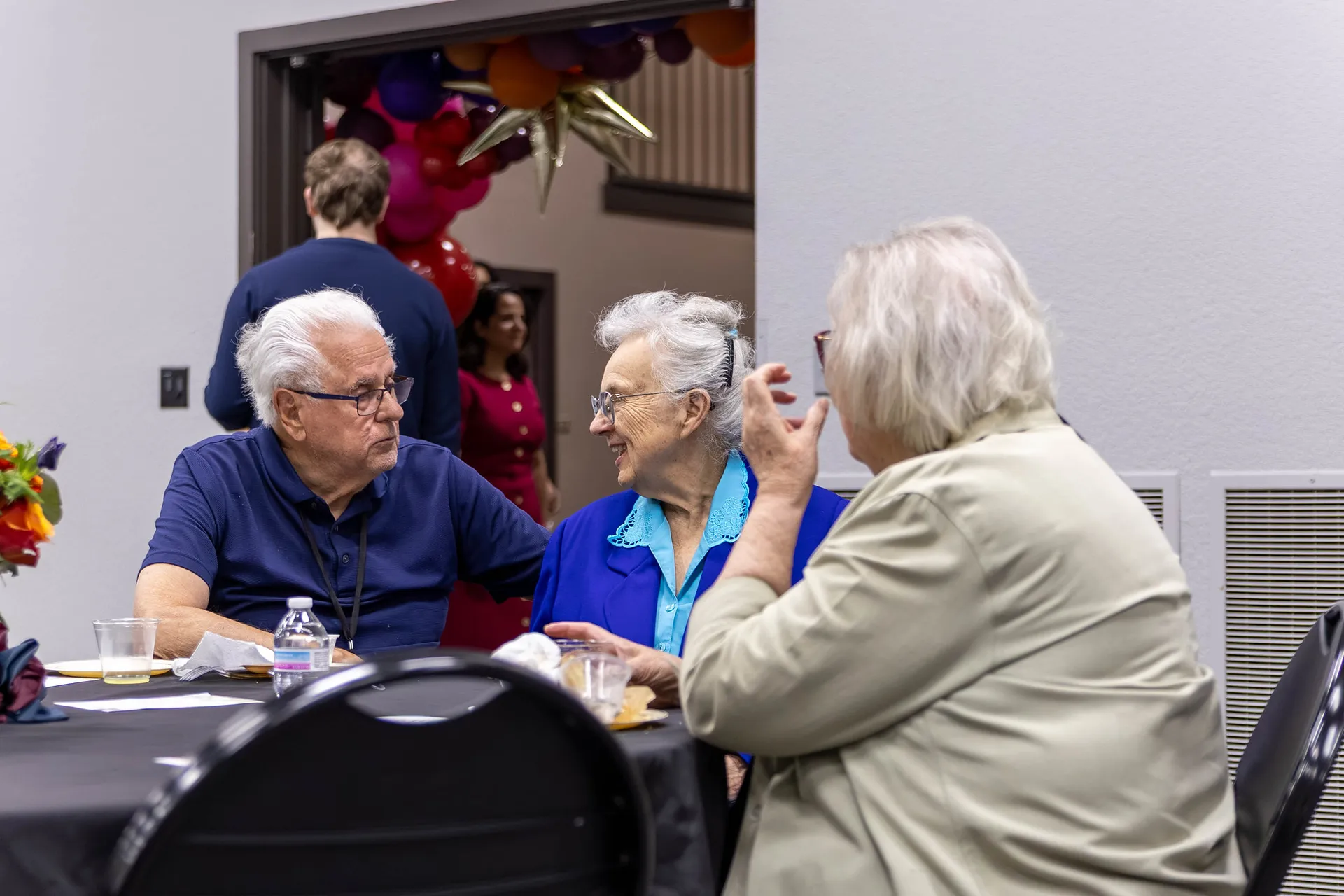 Three older alumni discussing at a table