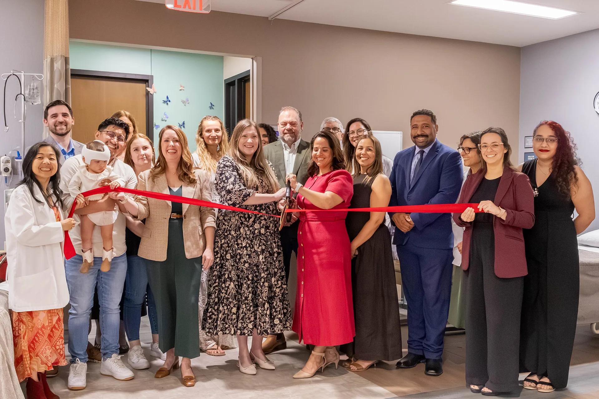 Group of alumni stand in front of red ribbon being cut by President Ana