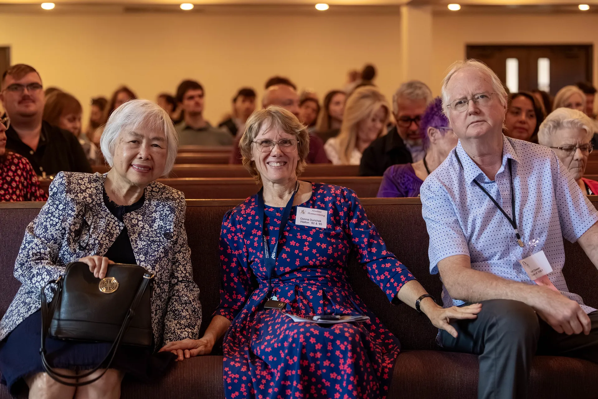 Three alumni sitting together on a church pew