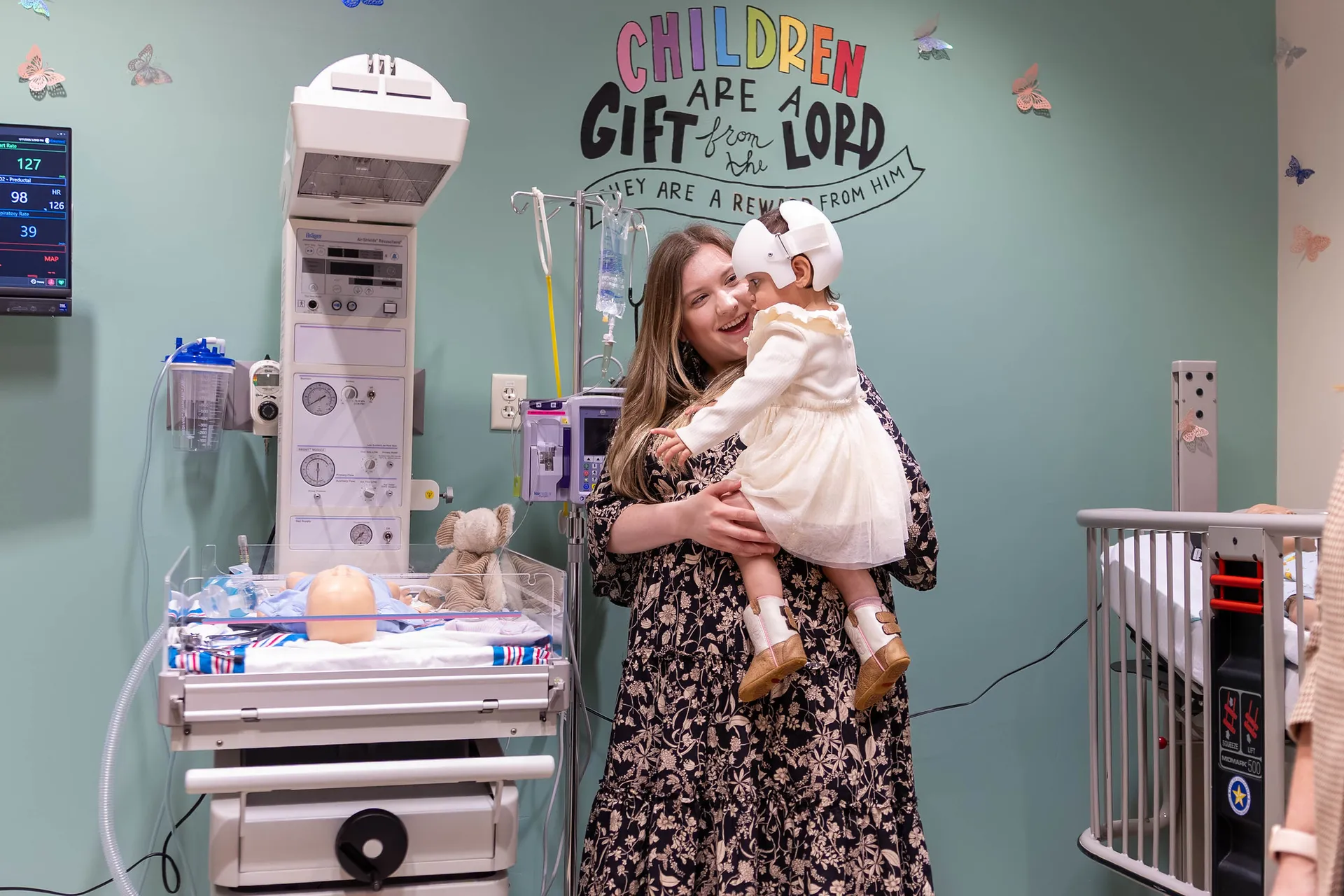Woman holding baby with white headgear, surrounded by nursing simulation equipment