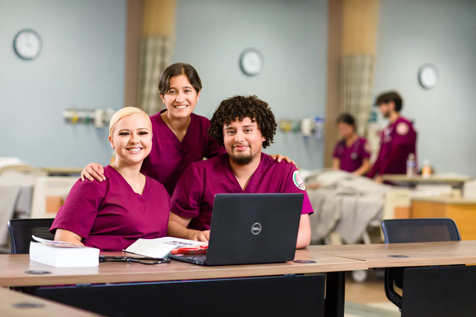 SWAU Nursing Students sitting in front of a laptop in a simulation lab smiling at the camera
