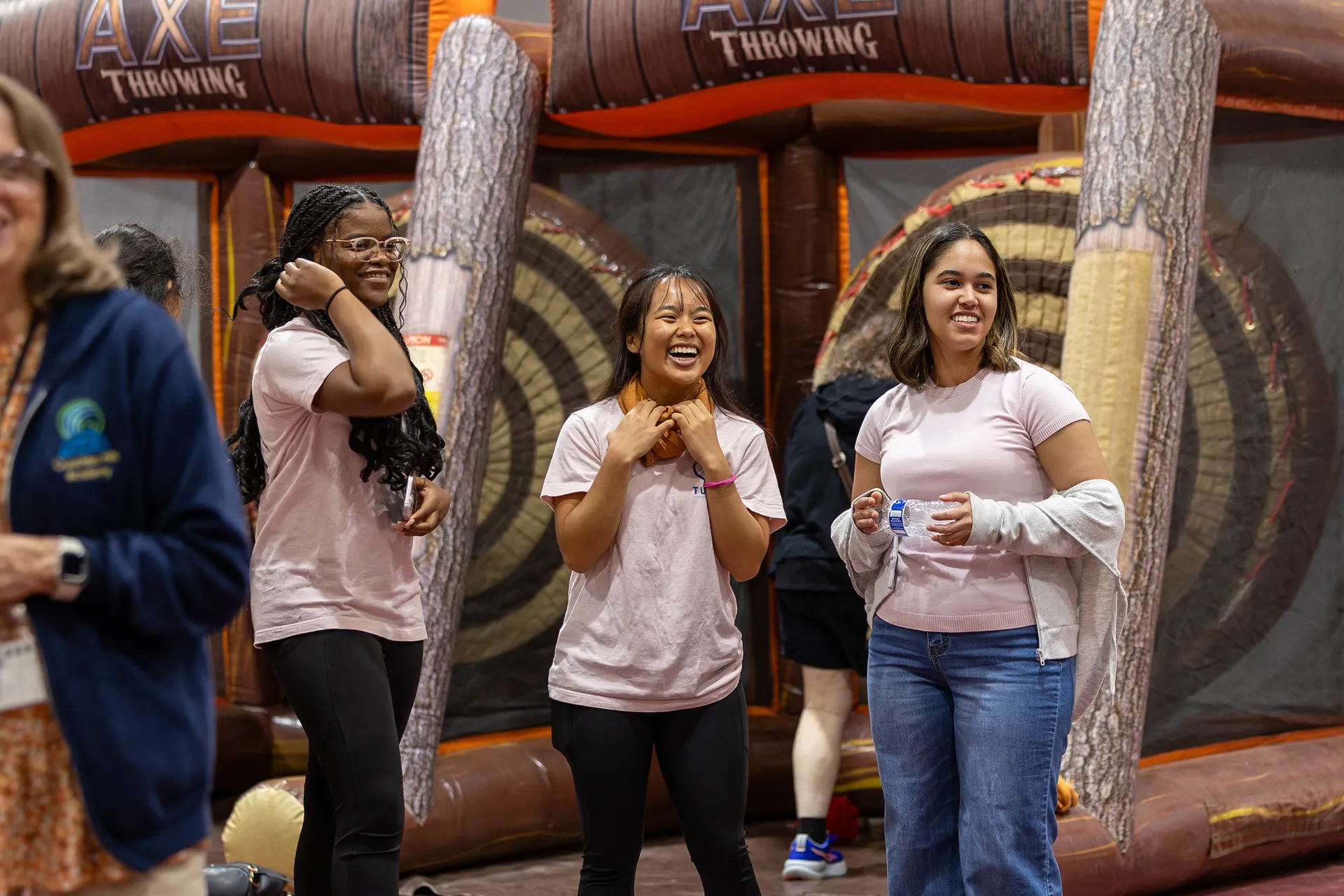 Three people smiling in front of a throwing axe booth