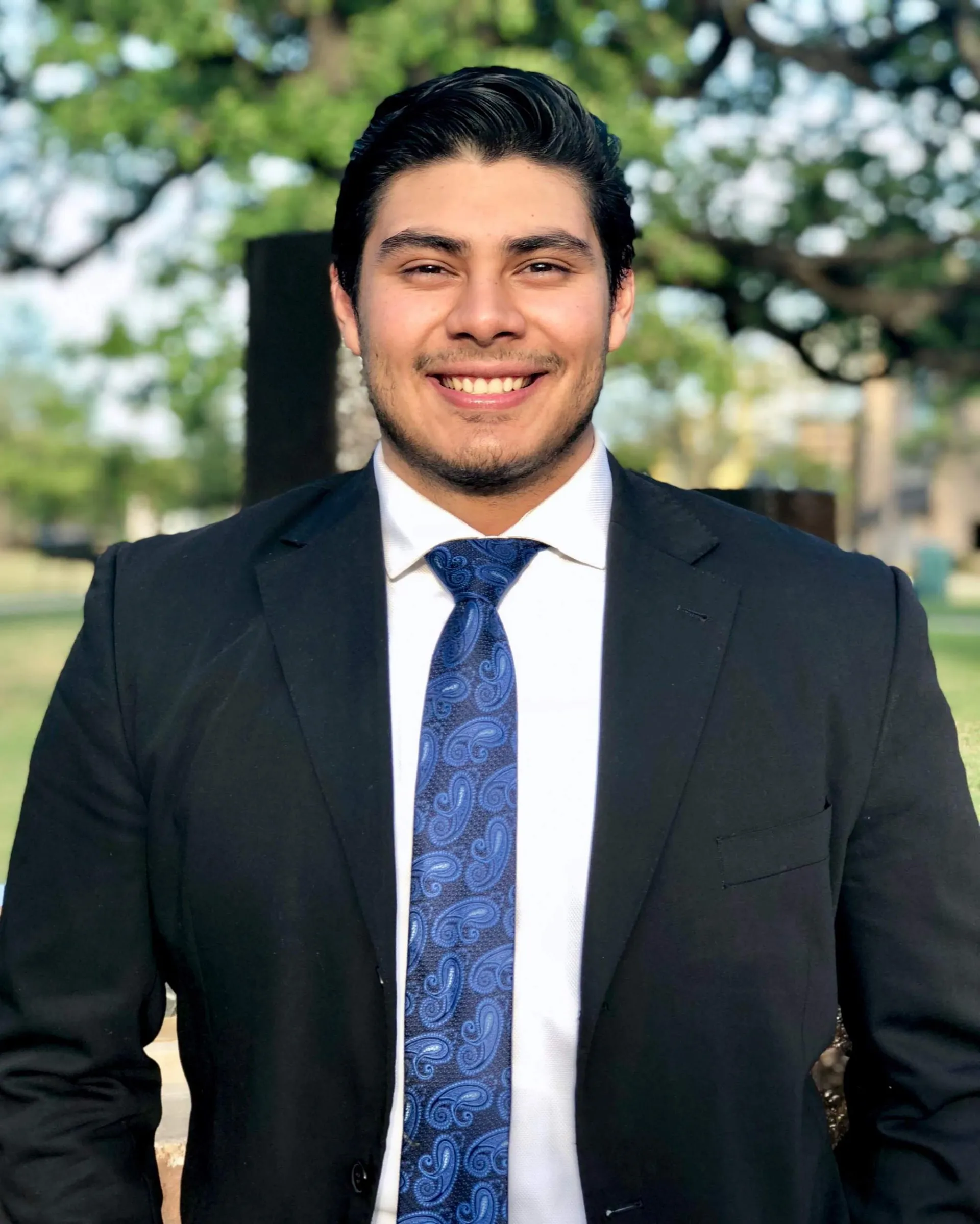 Josh in a suit and tie standing outside and smiling at the camera.