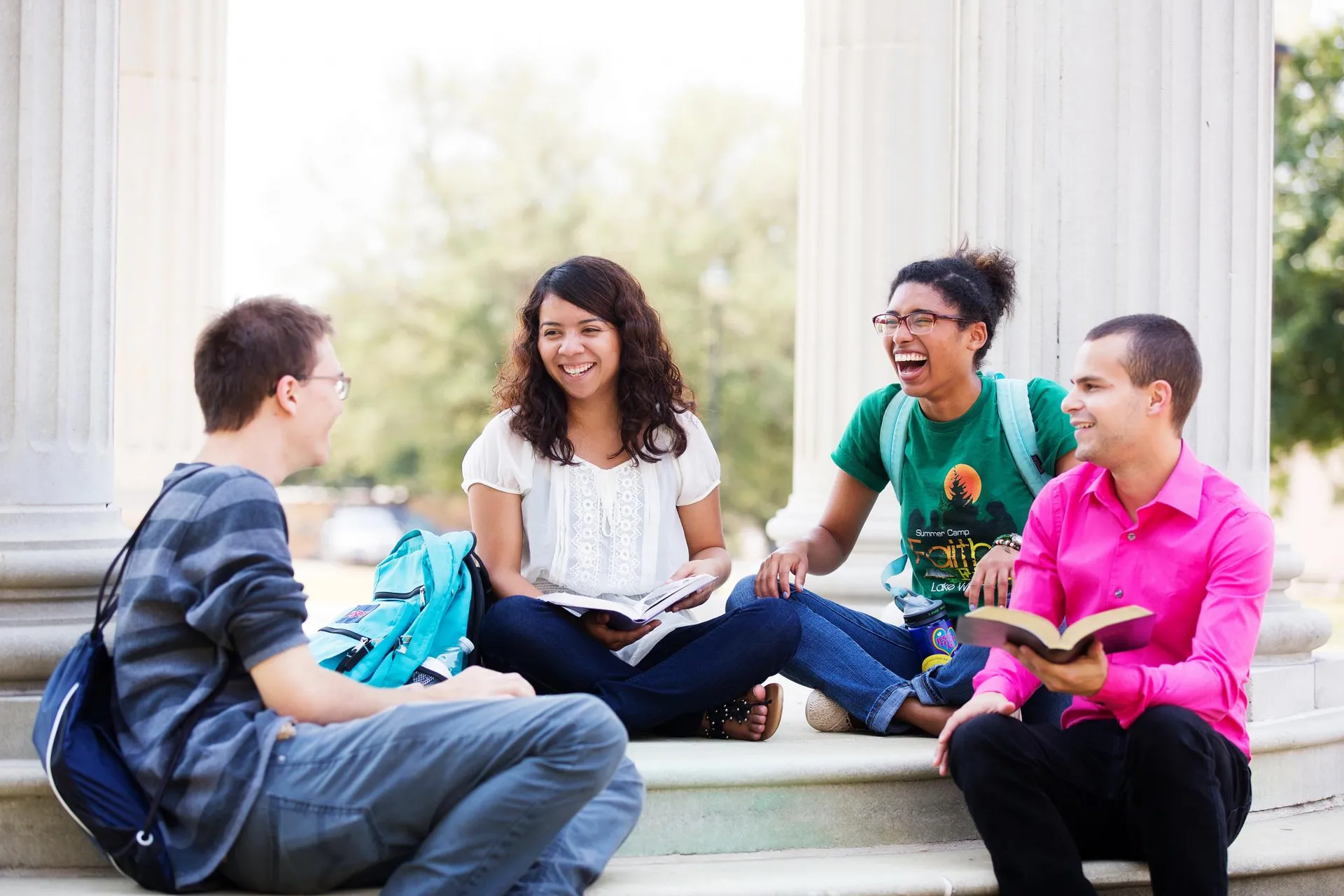 Four students smile and laugh as the sit at the bottom of the rotunda with their books and bags