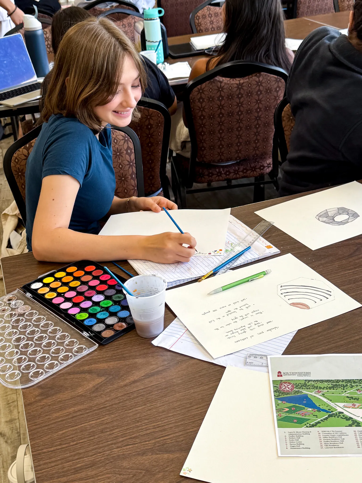 student sitting at table painting with watercolors