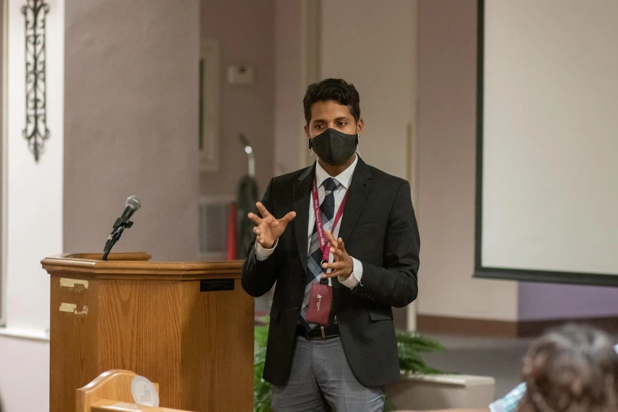 Man in suit wearing a mask and Southwestern Adventist University lanyard using his hands as he speaks