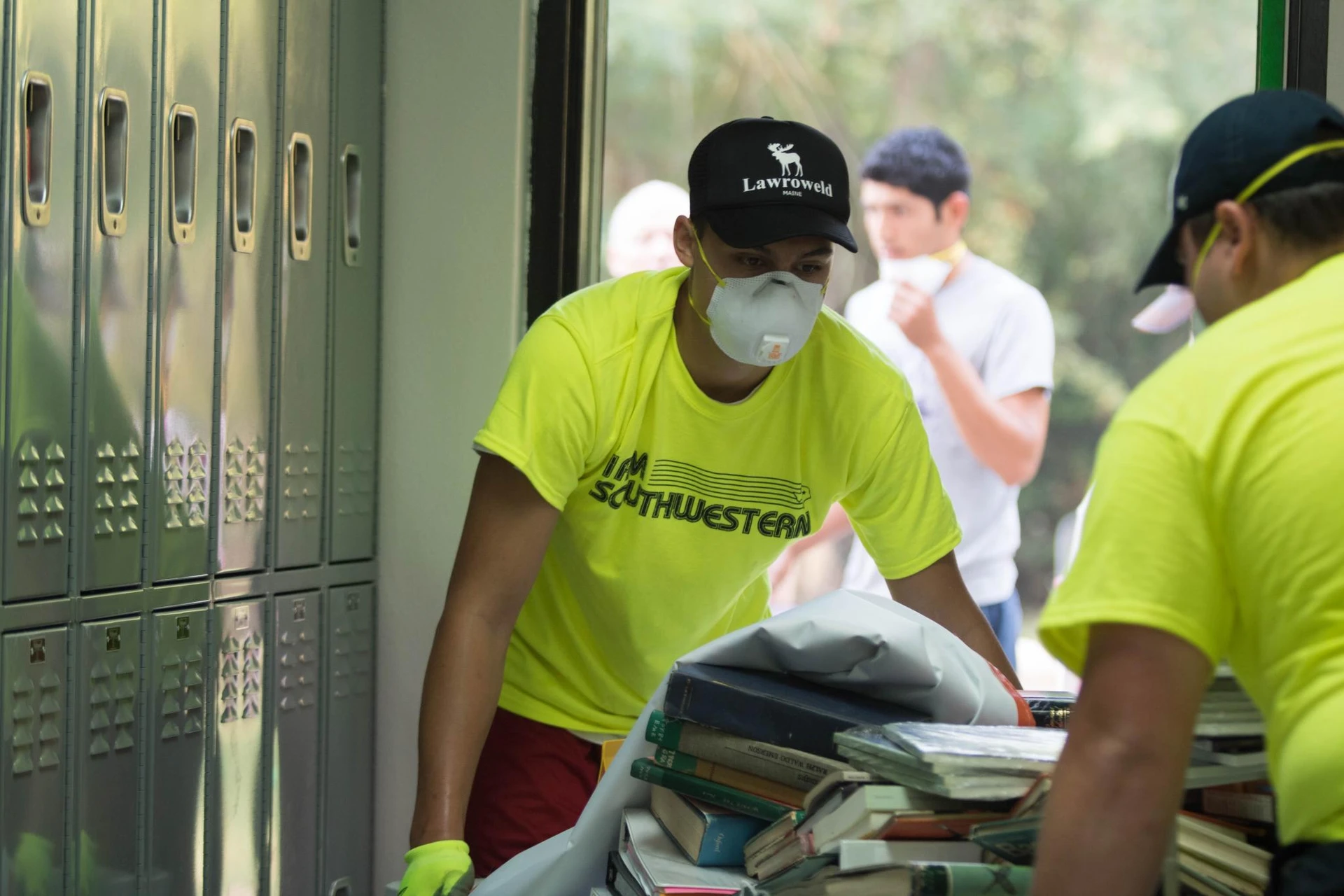 Students, dressed in matching highlight yellow t-shirts, wear white masks as they clean out some lockers